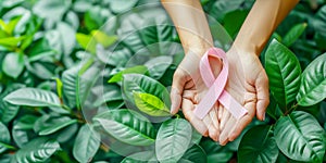 Two hands gently hold pink ribbon over lush nature background of green leaves