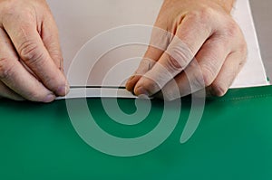 Two hands hold a green file folder with a binder on a gray surfa