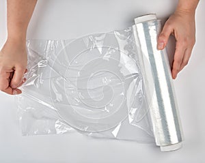 two hands hold a large roll of wound white transparent film for wrapping food