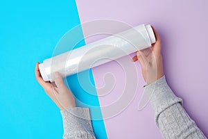 Two hands hold a large roll of wound white transparent film for wrapping food