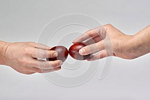 Two hands holding Easter eggs check their strength on a light background