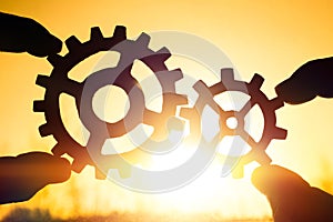 Two hands holding gears together. puzzle details on a sunset background.