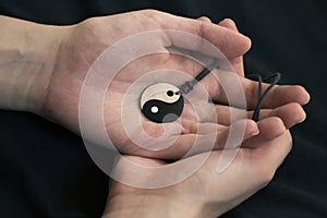 Two hands holding pearl yin yang necklace on dark background.