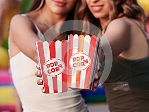 Two hands, holding popcorn in red and white paper boxes, Close-up picture of snack boxes at fun fair in theme park. Summertime