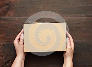 Two hands holding a rectangular cardboard box of brown kraft paper