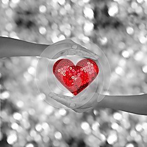 Two hands holding red heart shap on black and white bokeh