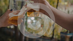 Two Hands Holding Transparent Plastic Cups With Light Beer And Cheers With Them