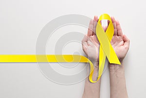 Two hands holding yellow ribbon, symbol of cancer