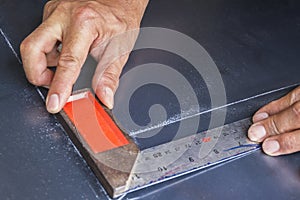 Two hands keep metal angle on steel plate.