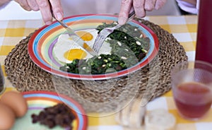 Two hands with knife and fork for eating eggs. Recipe with spinach, raisins and pine nuts. Healthy eating photo
