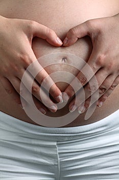 Two hands make a heart shape on pregnant belly