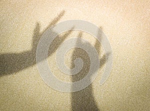 Two hands making shadow of I Love You sign on sand at the beach.