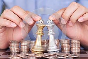 Two hands next to the dollar coin help the two chess kings duel