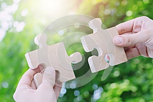 Two hands person trying to connect couple Jigsaw wooden puzzle piece with tree fresh background. one part of whole.