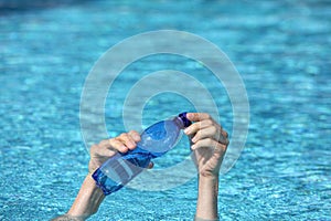 Two hands with plastic bottle of water above surface of water