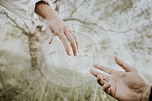 Two hands reach helping each other Against the background of a tree and grass