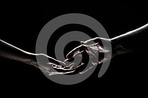 Two hands reaching toward. Helping hand outstretched for salvation on isolated black background. Close up of man and