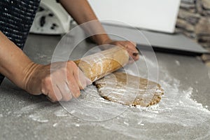 Two hands rolling, the biscuit dough evenly over flour with a rolling pin, making cookies and gingerbread in the kitchen