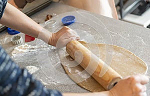 Two hands rolling, the biscuit dough evenly over flour with a rolling pin, making cookies and gingerbread in the kitchen