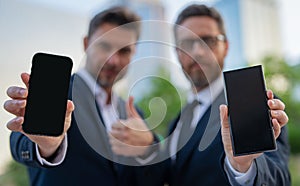 Two handsome businessman using phone and standing on the street outdoor. Portrait of a serious businessmen in formal