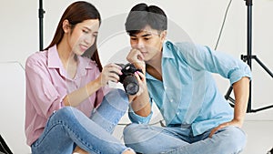 Two handsome man and beautiful woman wearing casual shirts smiling and looking or checking pictures in camera while sitting in