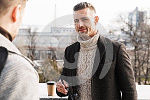 Two handsome men wearing coats spending time