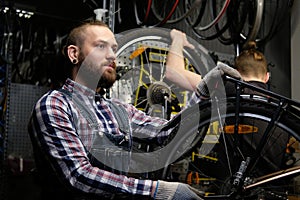 Two handsome stylish male working with a bicycle in a repair shop. Workers repair and mounts bike in a workshop