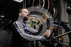 Two handsome stylish male working with a bicycle in a repair shop. Workers repair and mounts bike in a workshop