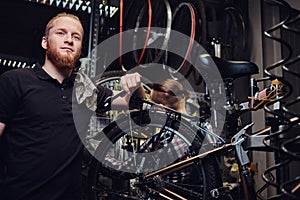 Two handsome stylish male working with a bicycle in a repair shop. Workers repair and mounts bike in a workshop