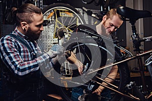 Two handsome stylish male working with a bicycle in a repair shop. Workers repair and mounts bike in a workshop