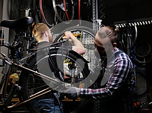 Two handsome stylish male working with a bicycle in a repair shop. Workers repair and mounts bike in a workshop