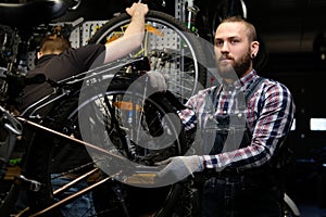 Two handsome stylish male working with a bicycle in a repair shop. Workers repair and mounts bike in a workshop