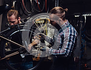 Two handsome stylish male working with a bicycle in a repair shop. Workers repair and mounts bike in a workshop