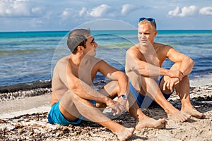 Two handsome young men chatting on a beach