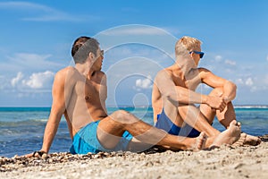 Two handsome young men chatting on a beach