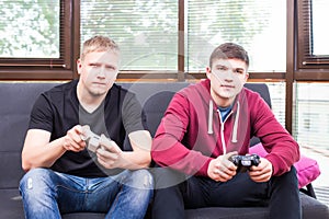 Two handsome young men playing video games while sitting on sofa