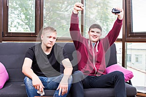 Two handsome young men playing video games while sitting on sofa