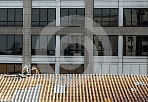 Two handyman workers repairing tiles on the damaged factory roof