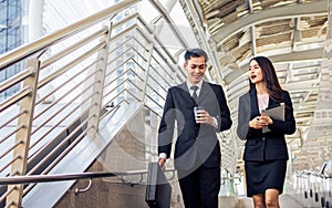 Two happy adult Asian businessman and woman or colleagues wearing formal suits, talking, walking together outdoor, going to work,