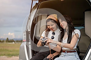 Two happy Asian female are checking the pictures on the camera, having fun during their road trip