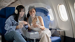 Two happy Asian female friends are enjoying talking during the flight for their vacation together