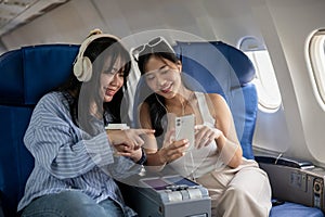 Two happy Asian female friends are enjoying talking during the flight for their vacation together