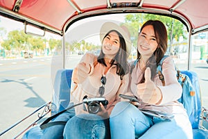 Two Happy Asian girls best friends traveler sit in Tuk Tuk taxi showing thumb up