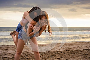 Two happy and attractive young Asian Chinese women girlfriends or sisters having fun playing in the sand on sunset beach in beauti