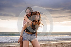 Two happy and attractive young Asian Chinese women girlfriends or sisters having fun playing in the sea on sunset beach in beautif