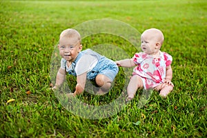 Two happy baby boy and a girl age 9 months old, sitting on the grass and interact, talk, look at each other.