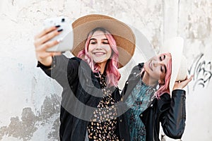 Two happy beautiful funny girls in fashionable denim clothes with a dress and hats take a selfie photo and enjoy a walk in the