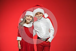 Two happy boy and girl in santa claus hats with gift boxes at studio