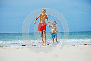 Two happy boys run on the sand beach holding hands