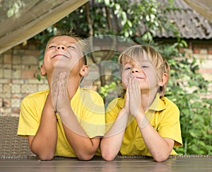 two happy boys in yellow t-shirts pray to God with their hands together